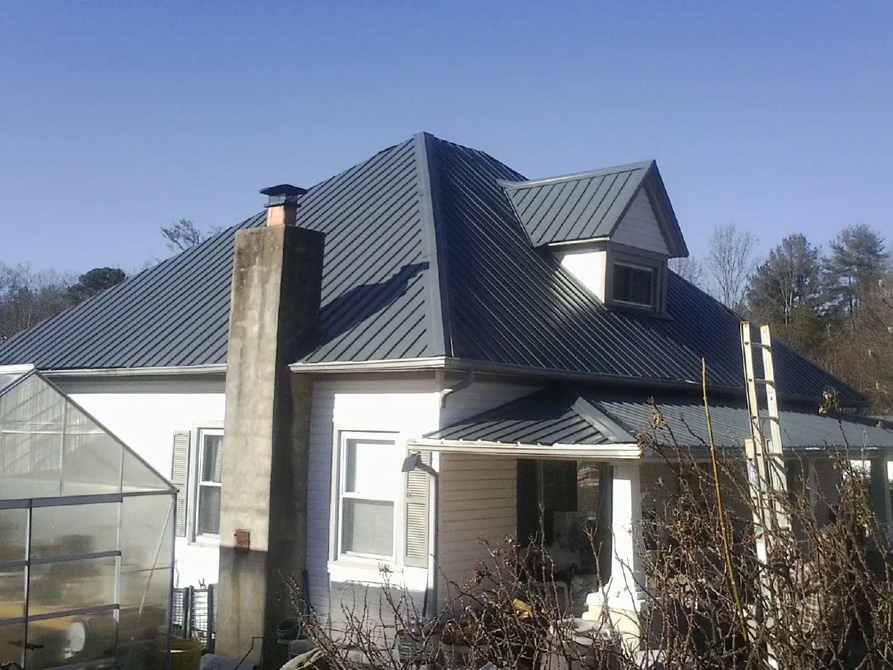 Dark blue standing seam metal roof on a white farmhouse with dormer — Slate & Tile Roof Repair by Roofing Brothers in Belmar