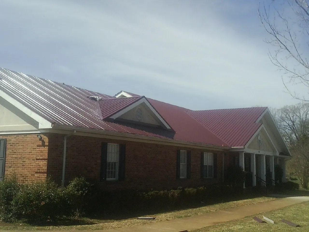 Red metal roof with gabled entries on a long brick building, from a Hail Damage Roof Repair job in Belmar
