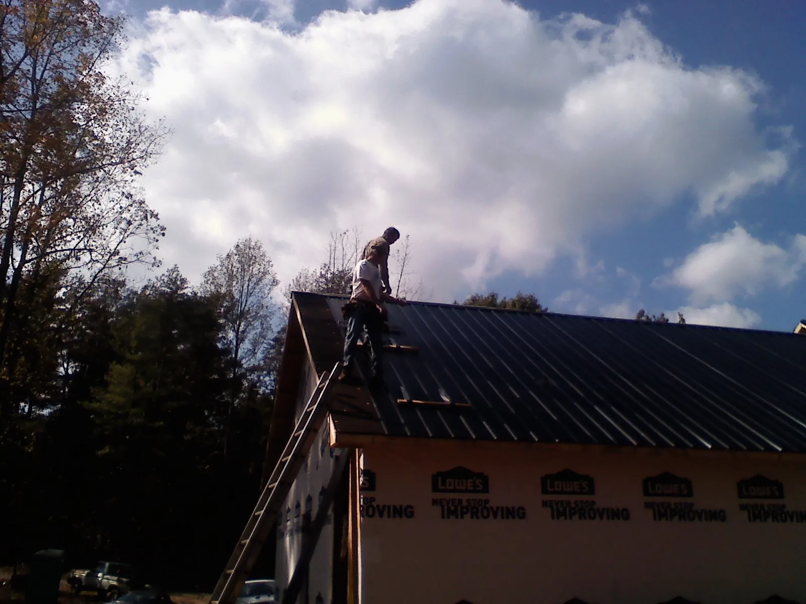 Roofer fastening dark metal panels high against a cloudy sky, from a Roof Inspection job in Belmar